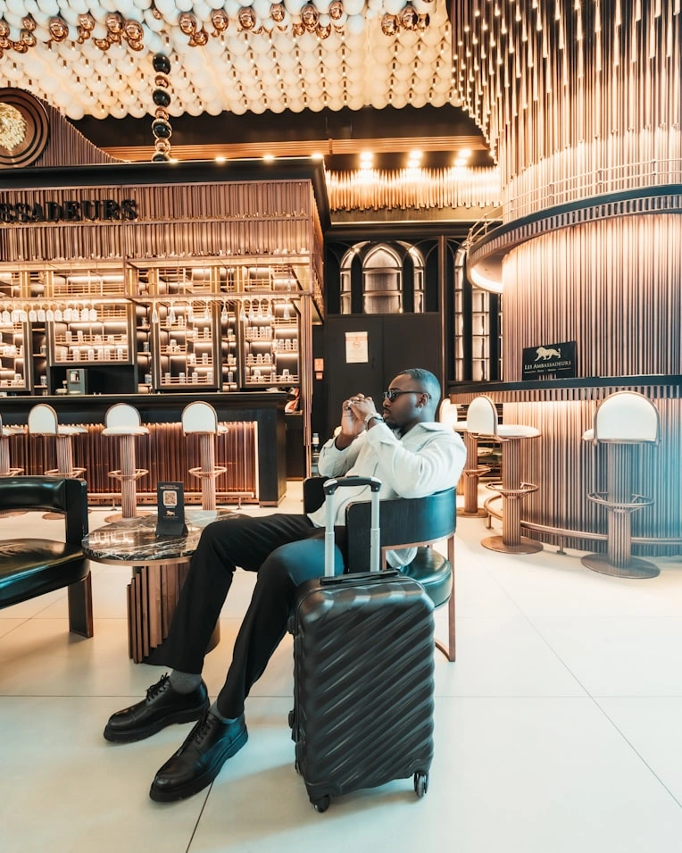 a businessman traveler sits confidently in a luxury hotel lounge dressed in monochrome tones with a sleek suitcase beside him