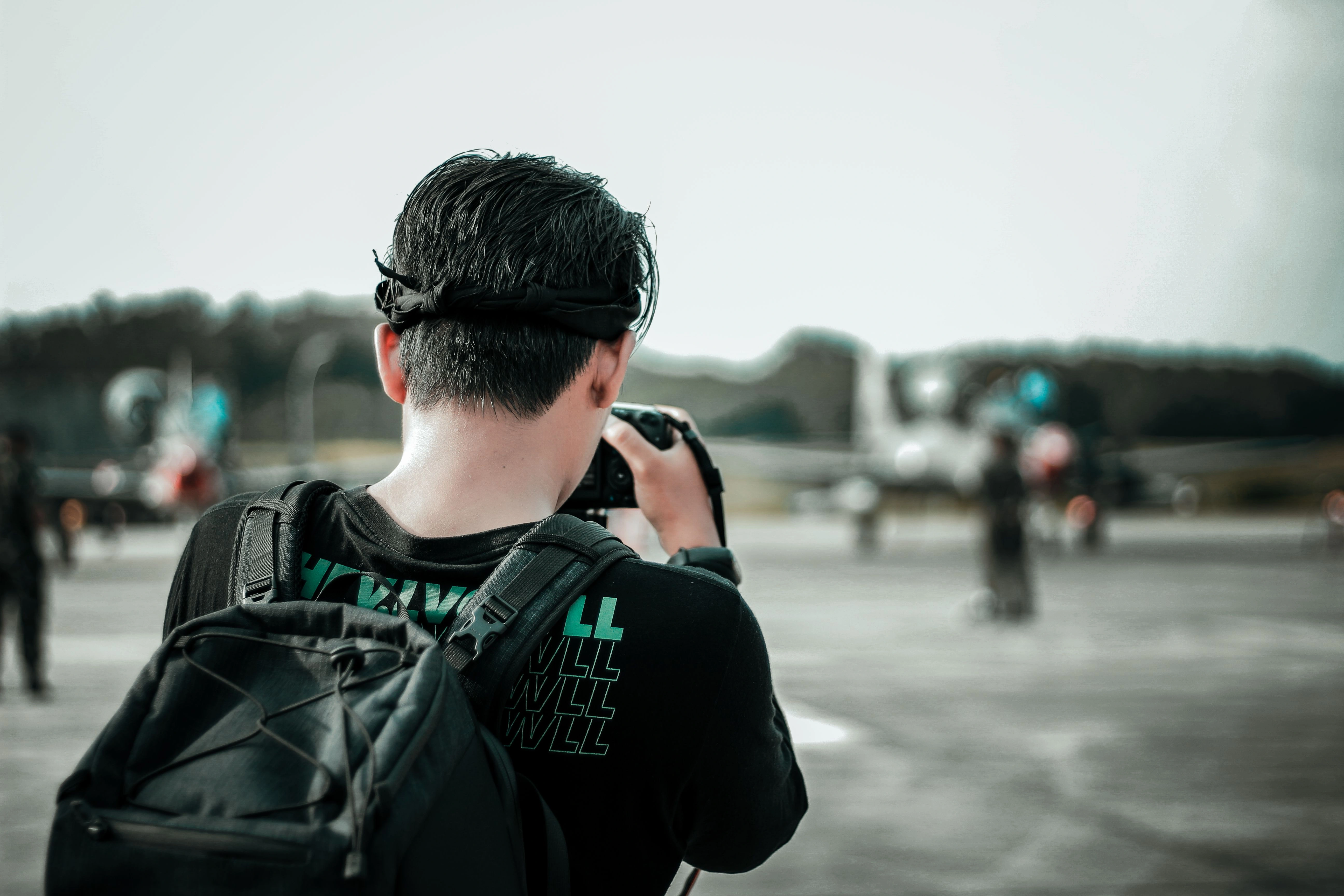 A man with a backpack photographs airplanes on an outdoor runway during the day at miami international airport