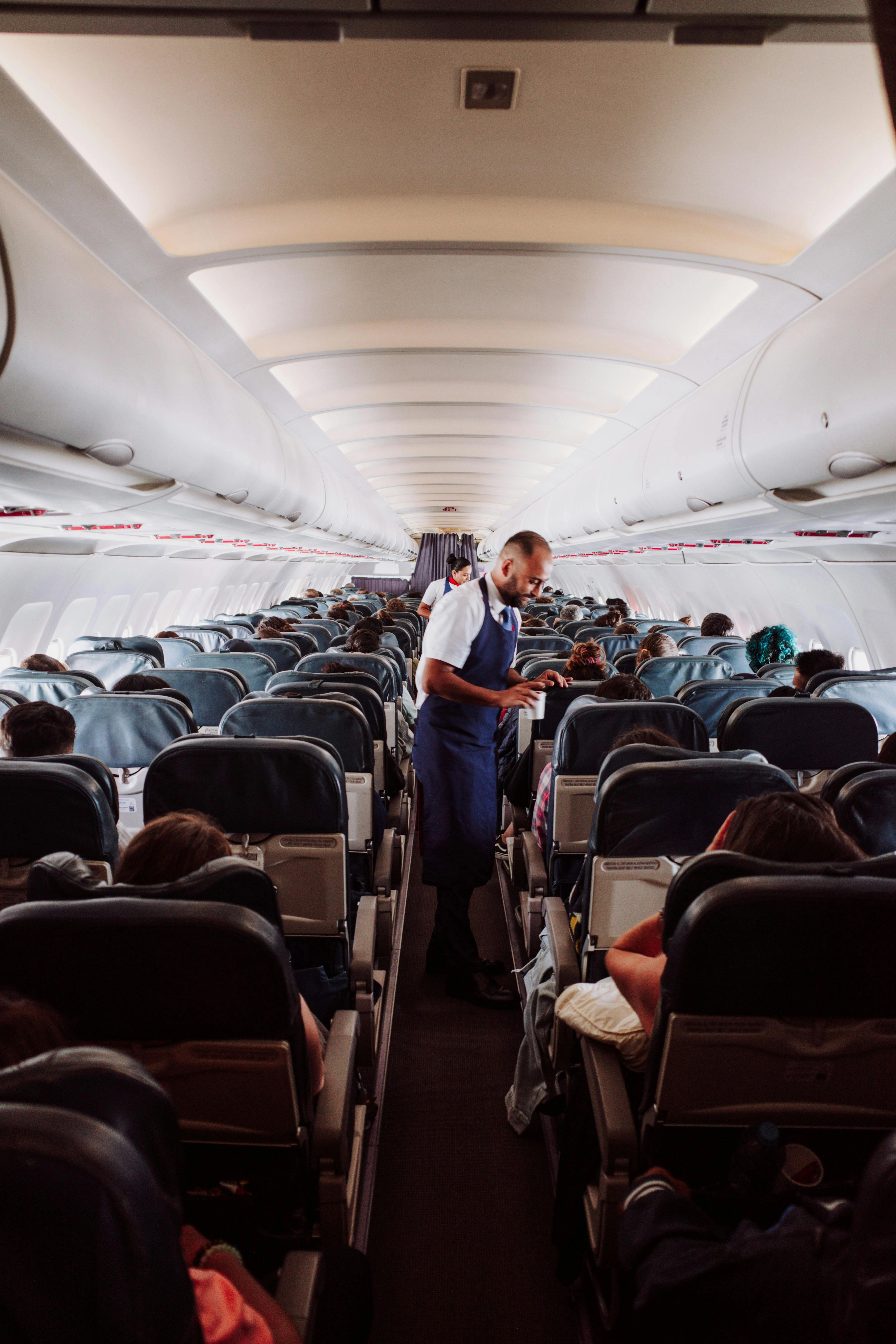 Flight attendant assists passengers in a crowded airplane aisle with rows of seats